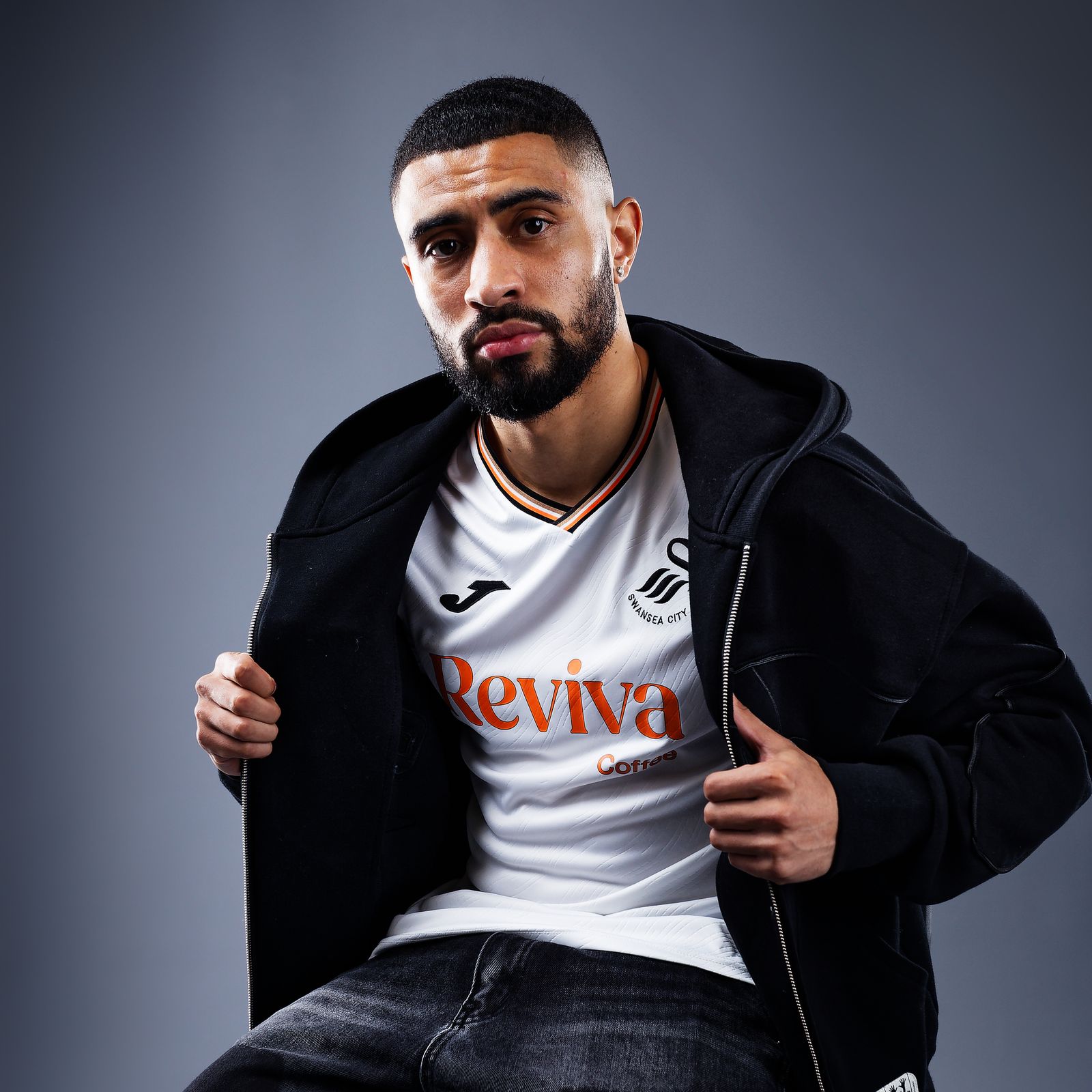 Footballer Josh Ginnelly poses in a home shirt during a studio shoot, for the 2024-2025 Championship football season, at the Swansea City AFC club shop, Swansea, Wales, UK